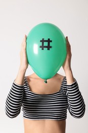 Photo of Woman holding green balloon with paper hashtag symbol in front of her face on white background