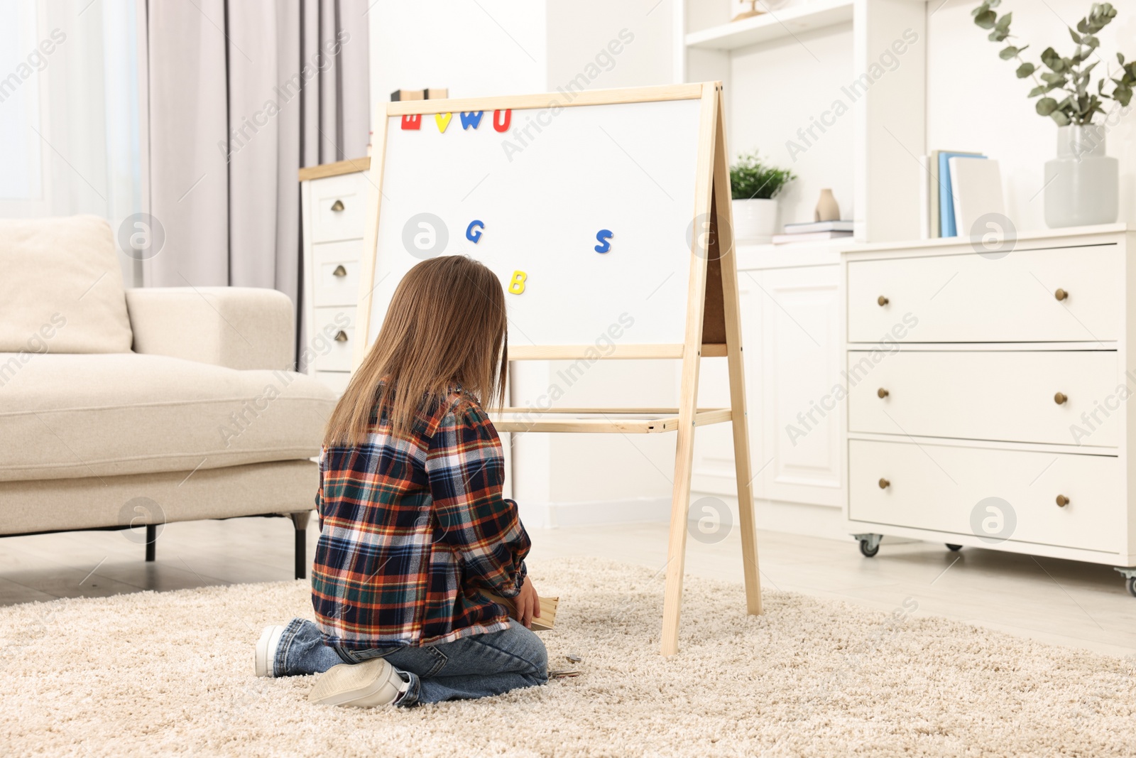 Photo of Cute little girl putting magnetic letters on board at home. Learning alphabet