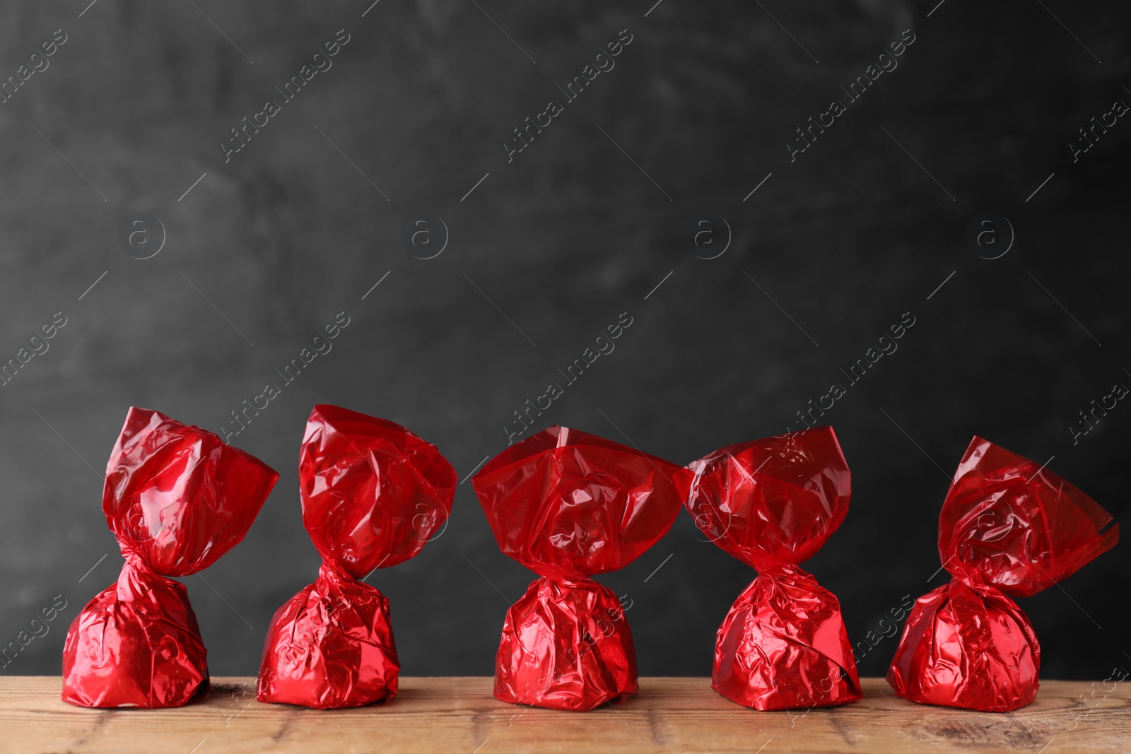 Photo of Delicious chocolate candies in red wrappers on wooden table
