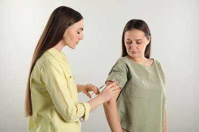 Photo of Woman giving insulin injection to her diabetic friend on grey background