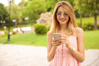 Young woman in stylish outfit with smartphone outdoors