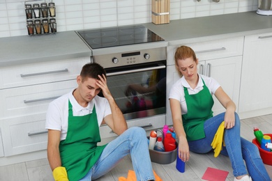 Photo of Exhausted janitors sitting on floor in kitchen. Cleaning service