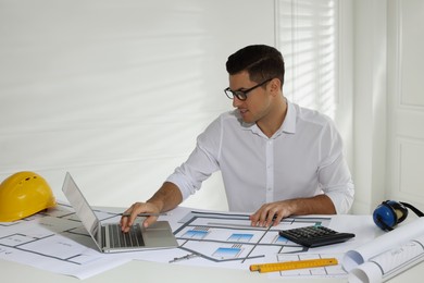 Architect working with construction drawings and laptop in office