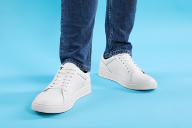 Photo of Man wearing stylish white sneakers on light blue background, closeup