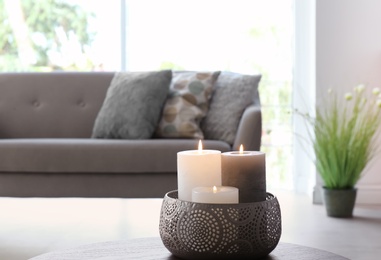 Vase with burning candles on table in living room