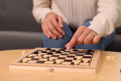 Photo of Woman playing checkers at wooden table, closeup