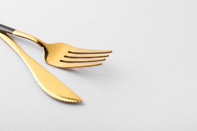Photo of Stylish cutlery. Golden knife and fork on gray background, closeup. Space for text