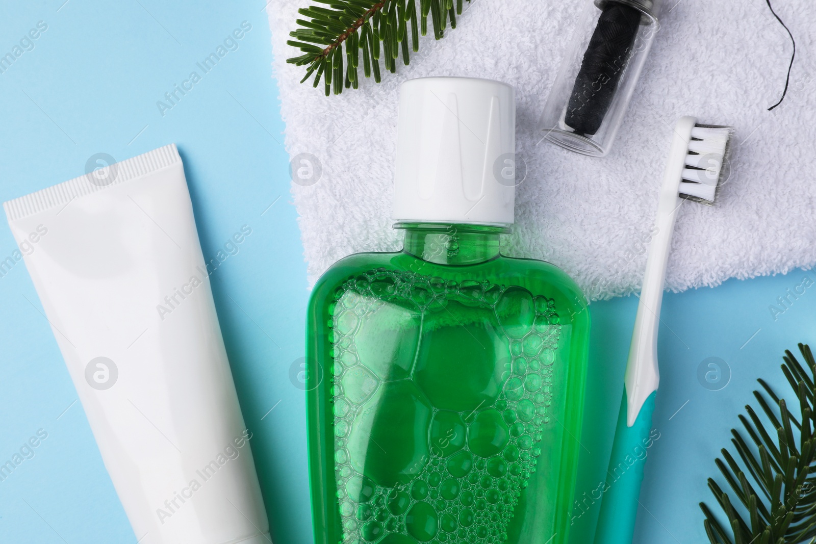 Photo of Fresh mouthwash in bottle, toothbrush, toothpaste and dental floss on light blue background, flat lay