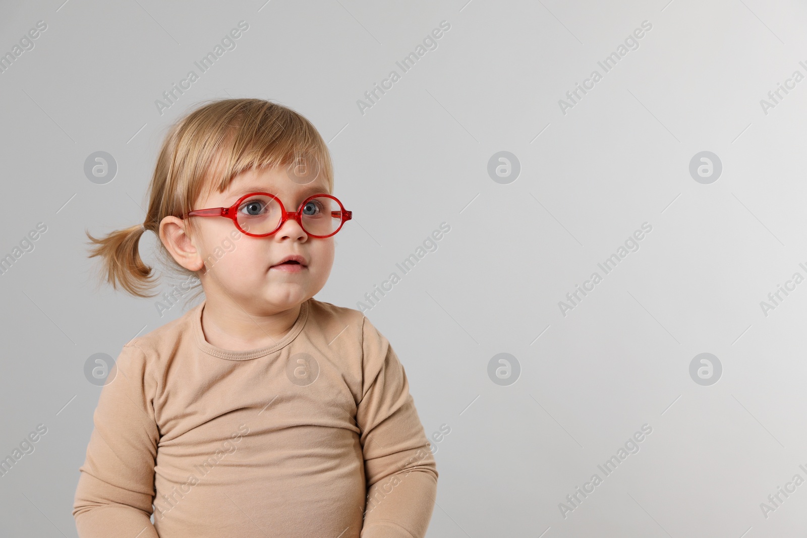 Photo of Cute little girl in glasses on light grey background. Space for text