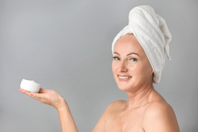 Portrait of beautiful mature woman with perfect skin holding jar of cream on grey background