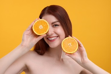 Smiling woman with freckles covering eye with half of orange on yellow background