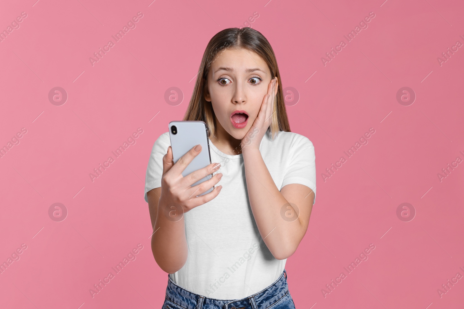 Photo of Shocked teenage girl with smartphone on pink background