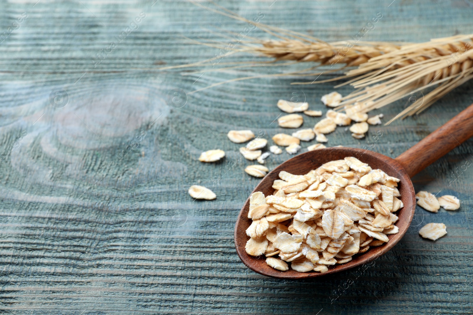 Photo of Spoon with oatmeal on light blue wooden table, closeup. Space for text