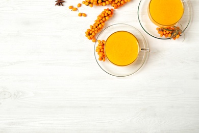 Photo of Delicious sea buckthorn tea and fresh berries on white wooden table, flat lay. Space for text