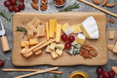 Photo of Cheese plate with honey, grapes and nuts on grey table, flat lay