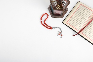 Photo of Muslim lamp, Koran and prayer beads on white background, top view with space for text