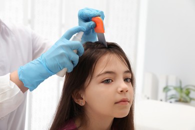 Doctor using nit comb and spray on little girl indoors. Anti lice treatment