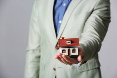 Male agent holding house model on grey background, closeup. Home insurance