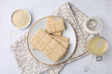 Delicious sweet kozinaki bars, honey and sesame seeds on white table, flat lay