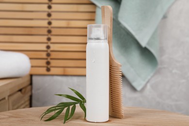 Photo of Dry shampoo spray, green leaves and comb on wooden table in bathroom