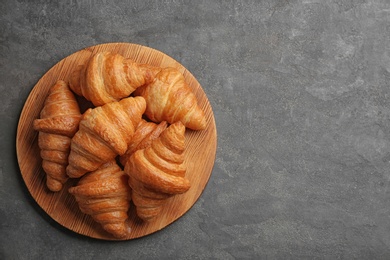 Photo of Wooden board with tasty croissants and space for text on grey background, top view. French pastry
