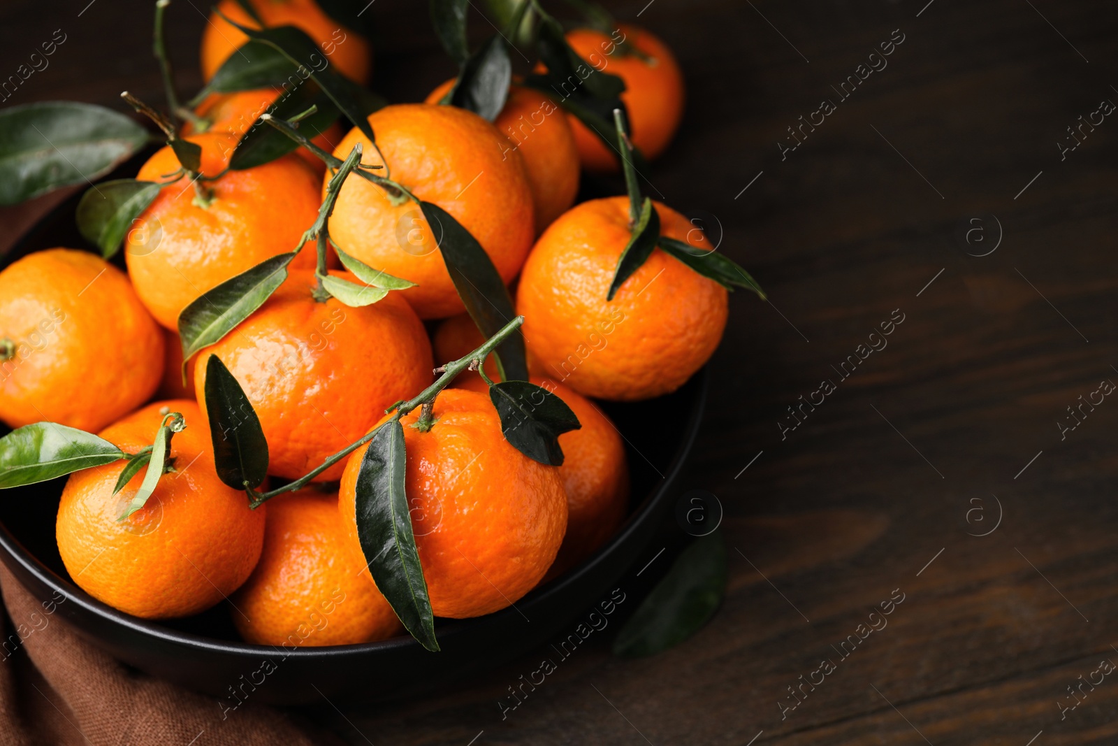 Photo of Fresh ripe tangerines with green leaves in bowl on table, closeup. Space for text