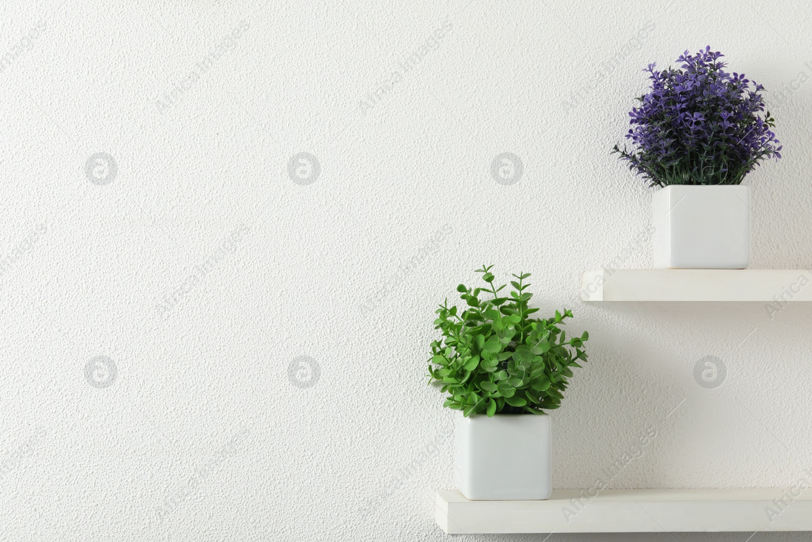 Photo of Beautiful artificial plants in flower pots on shelves. Space for text