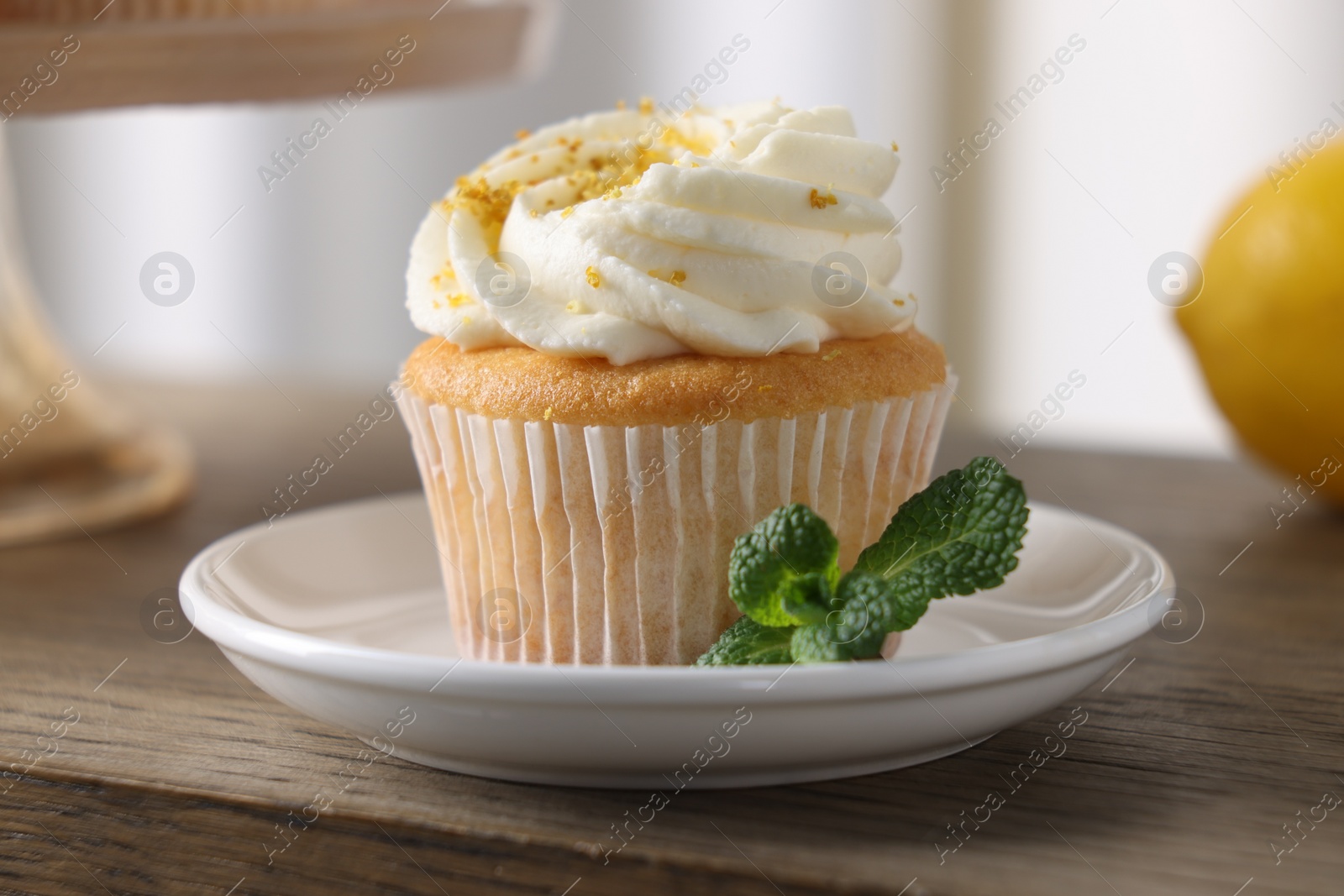 Photo of Delicious lemon cupcake with white cream and mint on wooden table, closeup