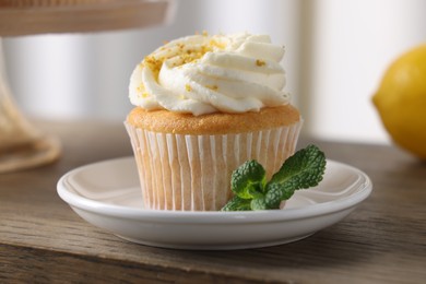 Photo of Delicious lemon cupcake with white cream and mint on wooden table, closeup