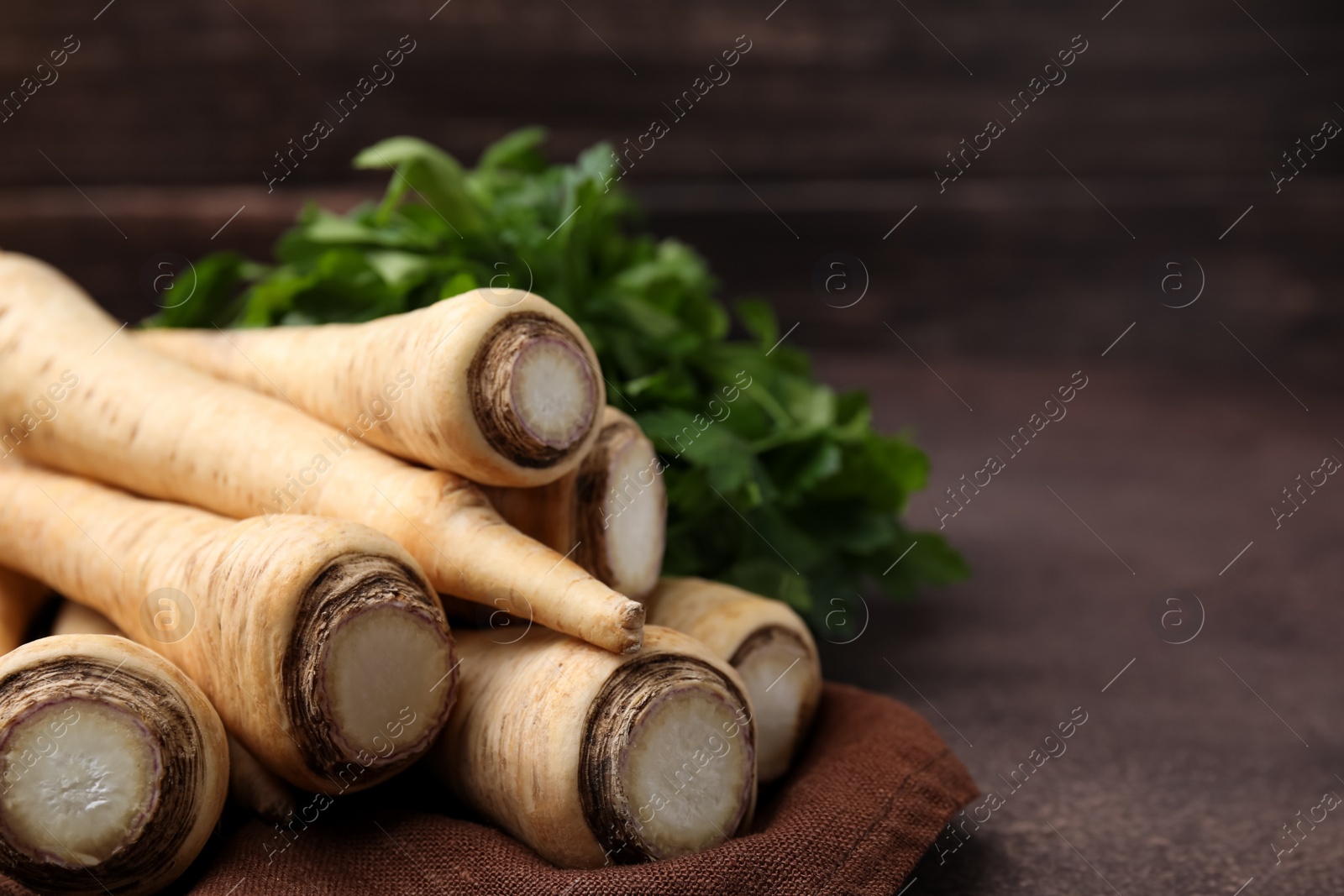 Photo of Whole raw parsley roots and fresh herb on brown table, closeup. Space for text