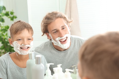 Father and son with shaving foam on faces in bathroom