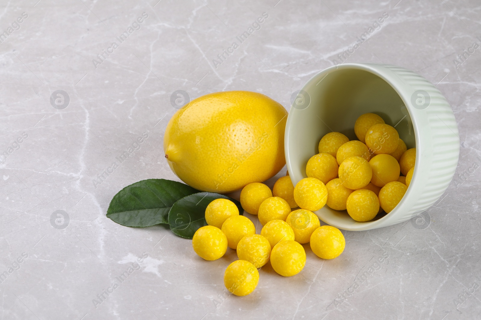 Photo of Tasty candy drops and fresh lemon on grey marble table