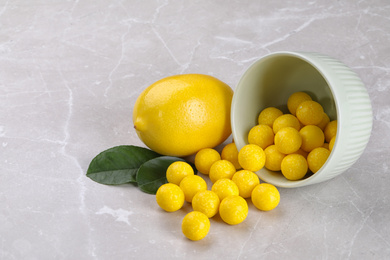 Photo of Tasty candy drops and fresh lemon on grey marble table