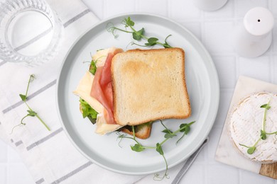 Photo of Tasty sandwich with brie cheese and prosciutto served on white tiled table, flat lay