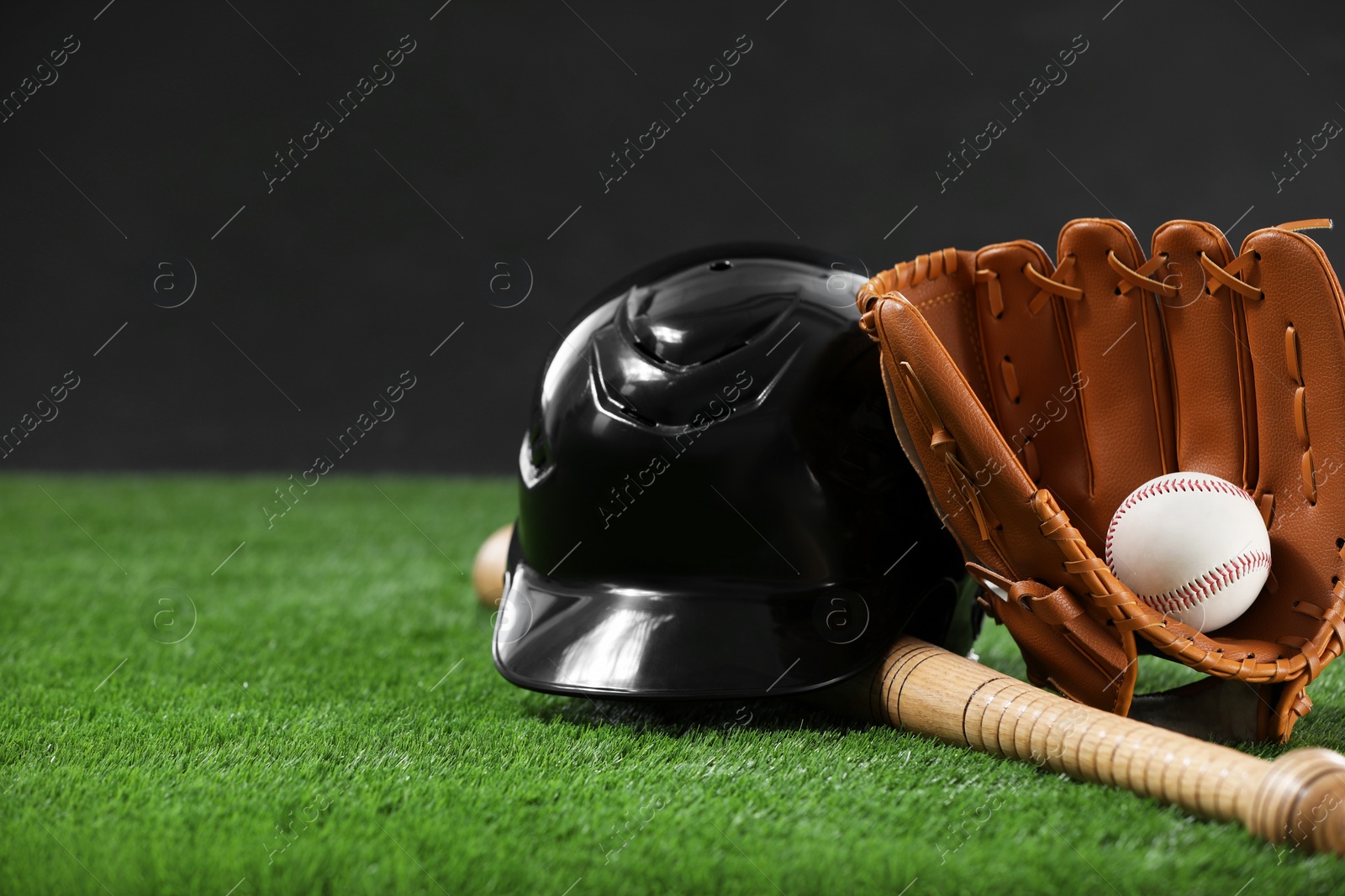 Photo of Baseball bat, batting helmet, leather glove and ball on green grass against dark background. Space for text