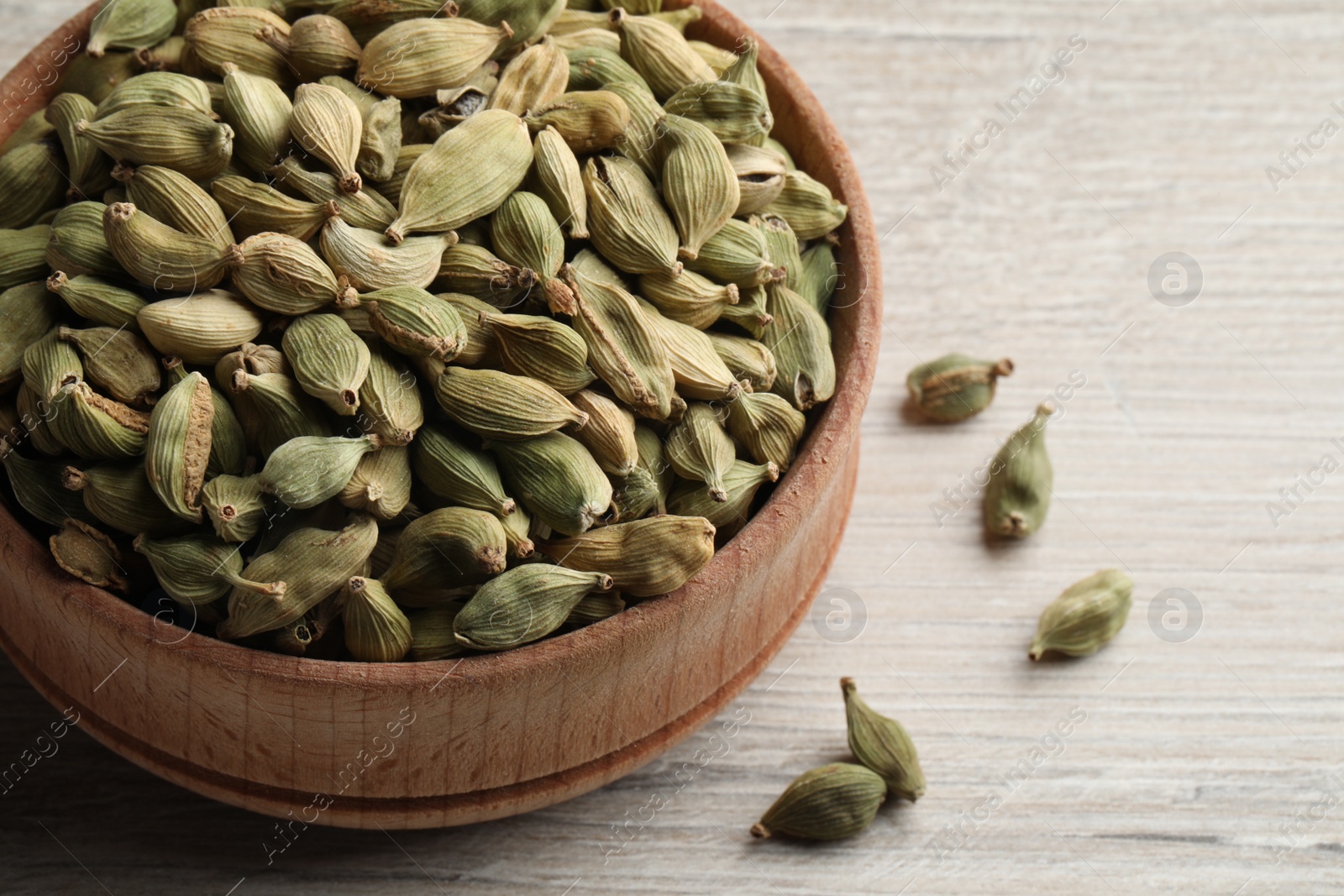 Photo of Bowl of dry cardamom pods on white wooden table, closeup