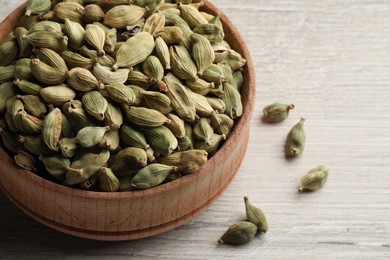 Photo of Bowl of dry cardamom pods on white wooden table, closeup