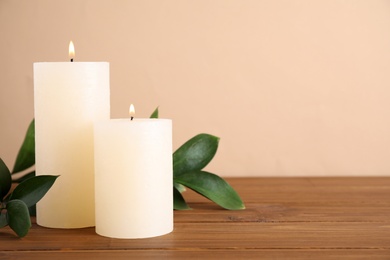 Photo of Burning candles with green branches on wooden table. Space for text