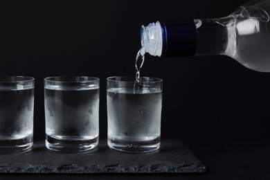 Pouring vodka from bottle in glass on black table