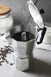 Brewed coffee in moka pot and beans on light grey table