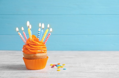 Photo of Delicious birthday cupcake with burning candles on table against color background