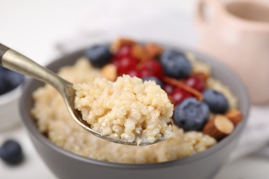 Photo of Spoon of delicious cooked quinoa above bowl, closeup