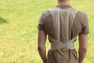 Photo of Closeup of man with orthopedic corset on green grass outdoors, back view. Space for text
