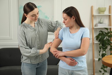 Woman giving insulin injection to her diabetic friend at home