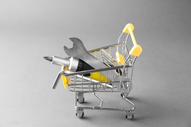 Photo of Small shopping cart with set of construction tools on grey background