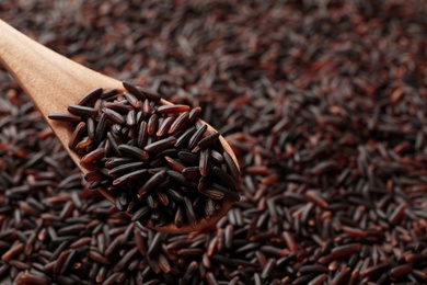 Wooden spoon with raw brown rice over cereal, closeup