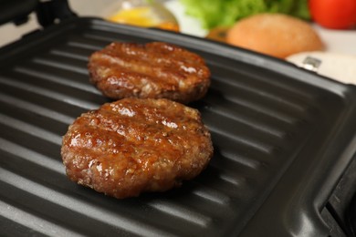 Delicious hamburger patties on electric grill, closeup