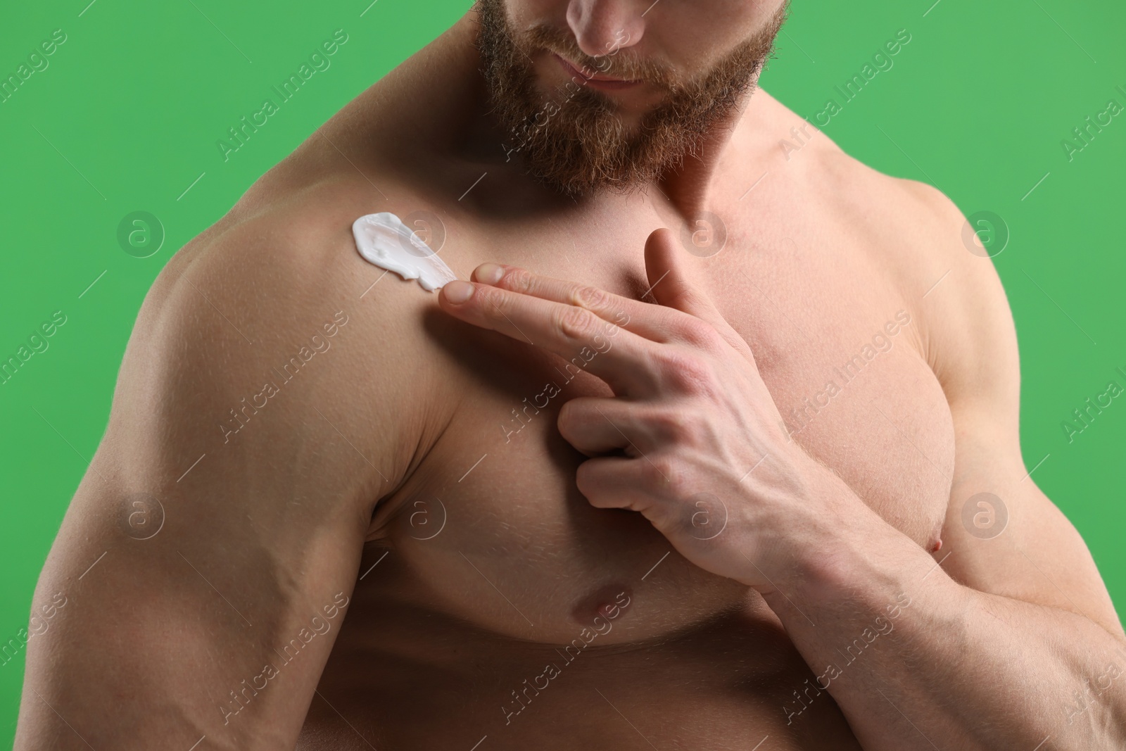 Photo of Man applying moisturizing cream onto his shoulder on green background, closeup