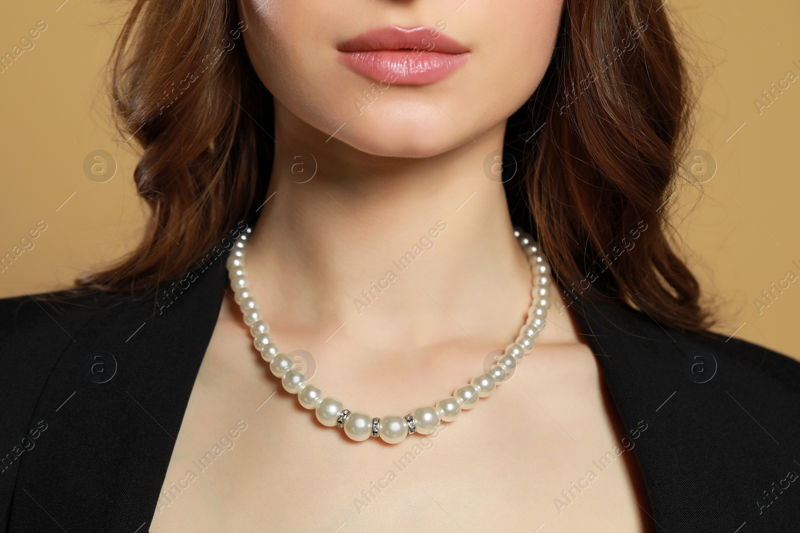 Photo of Young woman with elegant pearl necklace on brown background, closeup