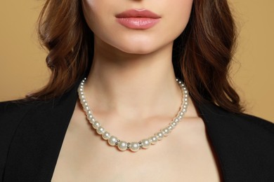 Photo of Young woman with elegant pearl necklace on brown background, closeup